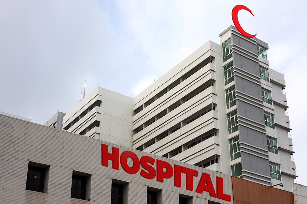 Modern hospital building exterior with prominent "hospital" signage, set against a cloudy sky.